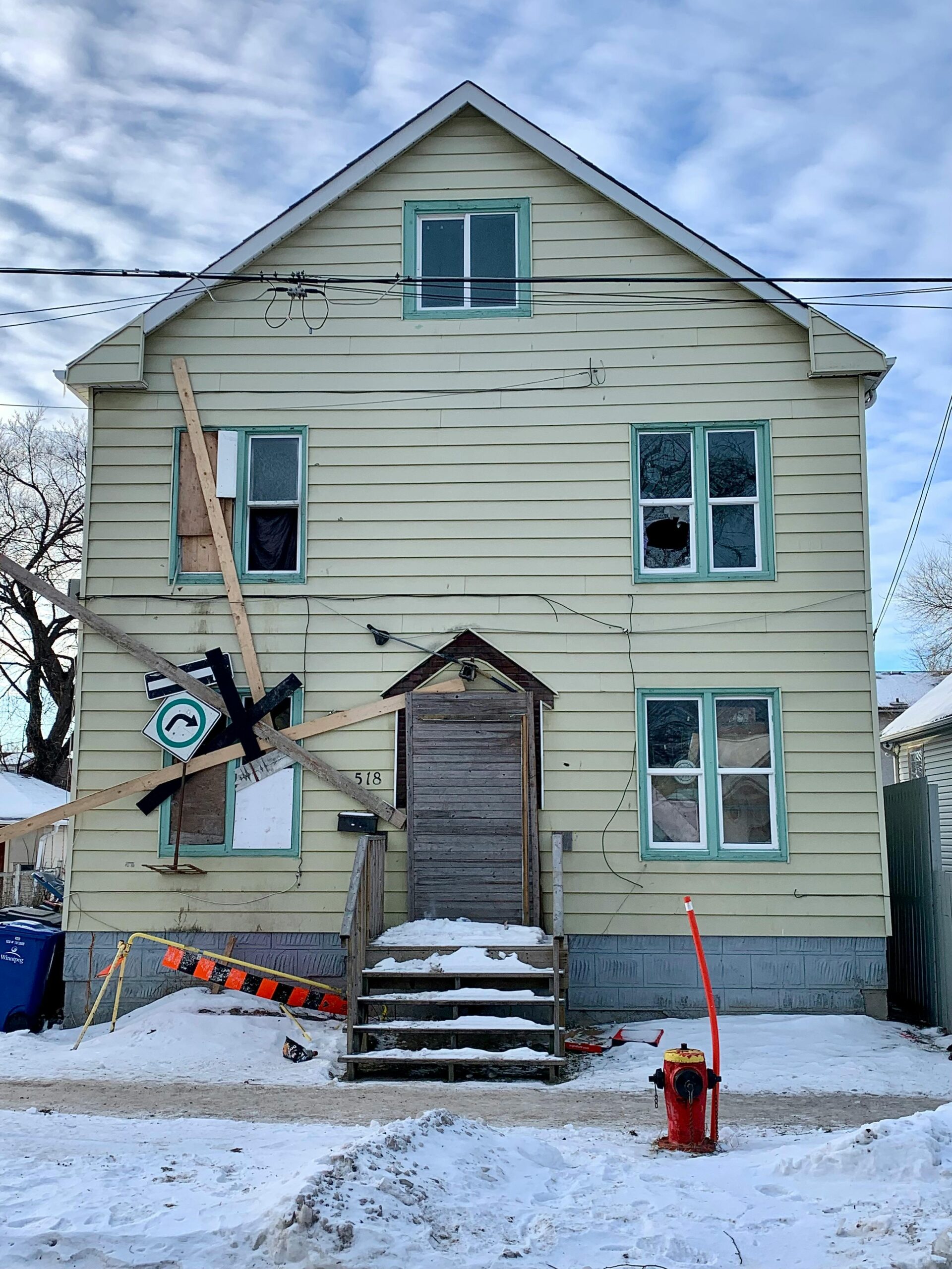 Boarded-up house in snowy Winnipeg, showing urban decay in winter.